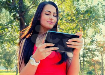 Toned image of female student using her tablet-pc outdoors. Beautiful Young Woman With Tablet Computer In Park