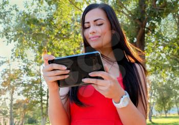 Female student using her tablet-pc outdoors. Beautiful Young Woman With Tablet Computer In Park