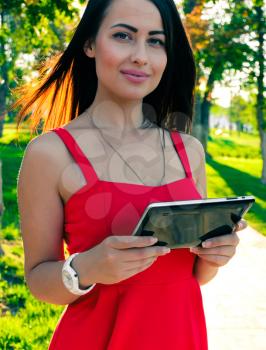 Beautiful Young Woman With Tablet Computer In Park looking at camera and smiling. Female student with tablet-pc in use