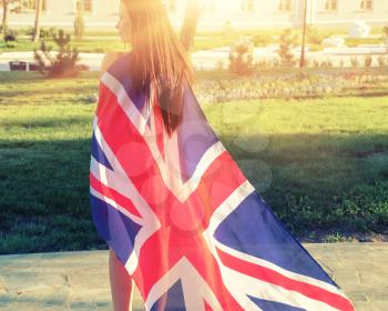 Young brunette warped in Great Britain flag like cloak from back view
