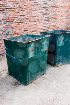 Angle vertical view of a two green dustbins outside against red brick wall