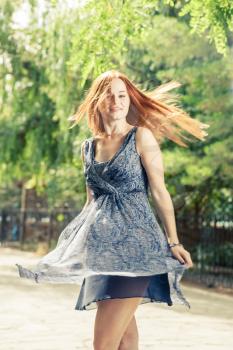 Young pretty women dancing in city park weared blue dress, toned image, blurred motion