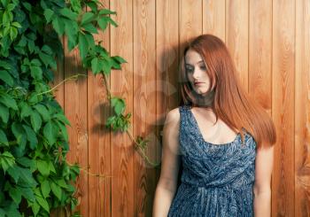 Red haired women leaning against plank fence with green ivy leaves.