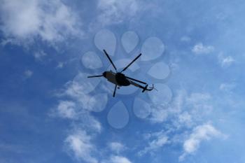 Silhouette of helicopter against blue sky with clouds