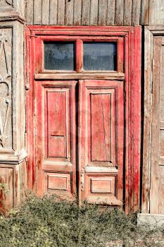 Aged red door with two glass windows on the top in old slum house in Astrakhan, Russia