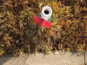 Plastic PVC pipe with red valve is set in dry grass near curbstone, water shortage, drought