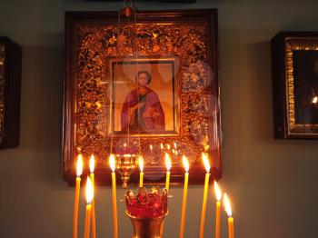 Astrakhan Russia - 10 October 2020: Orthodox church inside with burning candles on golden stand in front of the saint icon decorated with ornate golden frame.