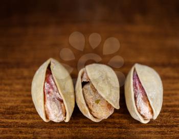 Macro Shot of Three Pistachio Nuts on dark wooden Background.