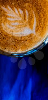 Latte art on the top froth of the flat white coffee servrd in small glass on blue background, top view