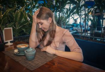 Heartbroken girl is sitting in cafe leaning head on hand.