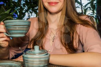 Partial view of lady holding cup of coffee in hands in an air in cafeteria