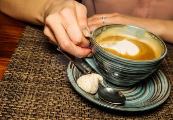 Mug of coffee on a cafe table, the girl holds in her hand one cup of milk coffee with froth art in an air. A photo depicting a cosy relaxing coffeebreak