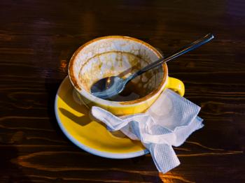 Empty coffee cup with spoon and smashed paper napkin on dark wooden tabletop at coffee shop