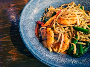 A bowl of delicious udon noodles with shrimps and vegetables, copyspace on table
