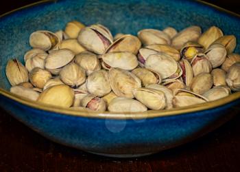 Pistachios kernel with open shells in a ceramic bowl in a vintage photo with harsh vignette. Pistachio is a healthy vegetarian protein source. Natural nuts snacks.