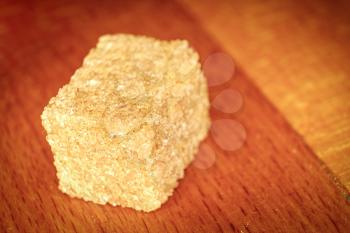 A cube of soluble brown sugar lies against a background of wood. Brown sugar is more healthy. There is a free place for text