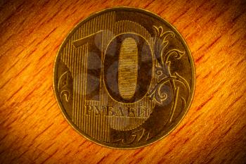 Ten rubles coin with inscription in Russian language - 10 rubles, macro picture on wooden background with vignette. Depicting slang name for ruble - wooden (currency).
