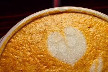 White heart shape on frothy top of latte coffee in cup