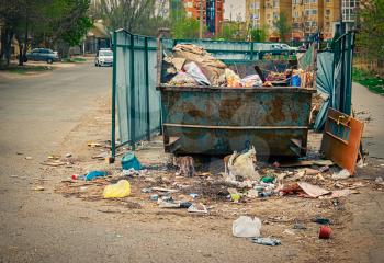 Overfilled trash dumpster in ghetto neigborhood. A lot of litter about.