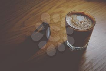 Coffeee cup on wooden table with sunglasses lying near, vintage low-light shot image