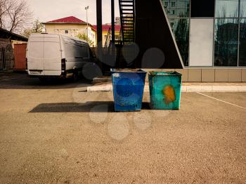 trash dumpsters rusty. Dustbins full of litter near office building with new commercial van on background.