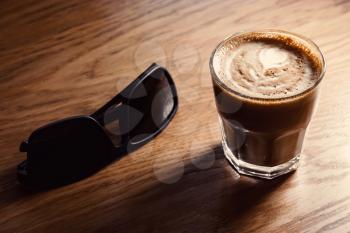 Sunglasses and flat-white coffee glass lying on wooden table