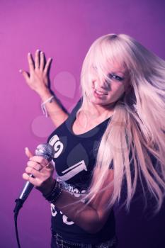 Karaoke singer woman blond hair with hair in motion on pink background sing in mic