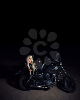 Young sexy fashionable blond haired lady lying on motorcycle bike in the night dark background, copyspace on top