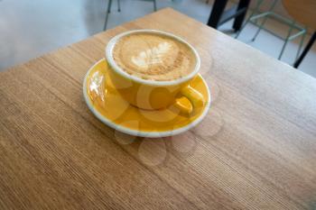 Yellow coffee cup with latte art served on table corner. Minimalistic composition.