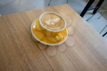 Yellow cappuccino cup with latte art served on table corner. Minimalistic composition.