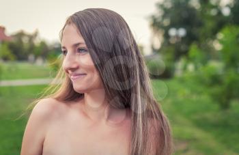 Photo of smiling millennial blond lady with bare shoulders posing outside in park with happy expression on her face looking aside camera.