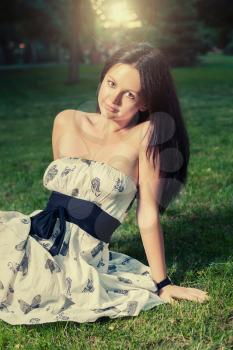 Brunette sitting on grass and looking at camera