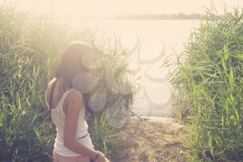 Backlit silhouette of girl alking towards the pond with reeds candid shot with flares low contrast, joy and fun in summer, summertime mood.