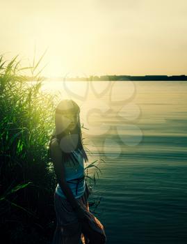 Melancholy solitude in deserted place. Lonely girl standing in reeds aside the pond