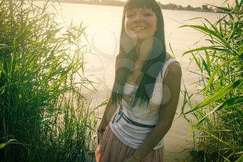Vintage photo of happy young woman in nature aside the river or pond low contrast backlit shot.