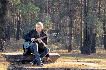 teen musician plays the guitar in the autumn forest