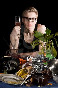A young man with a glass sits behind dirty table