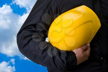 Royalty Free Photo of a Yellow Helmet at Builder Hands Against a Blue Sky