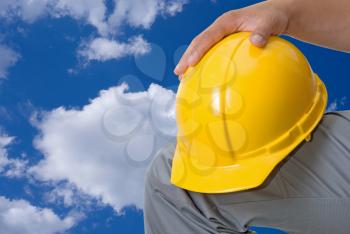 Royalty Free Photo of a Yellow Helmet at Builder Hands Against a Blue Sky
