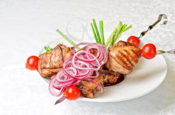 Grilled kebab meat with onion and tomato on a white plate