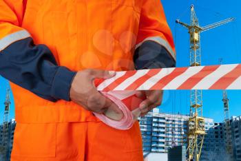 Worker stretch warning tape on building background