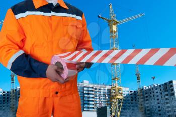 Worker stretch warning tape on building background