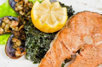 Tasty dish of salmon steak with algae mussels, lemon and kiwi