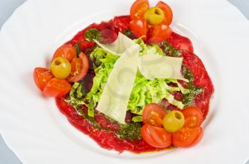 Meat carpaccio from beef meat, parmesan cheese, olive, tomato, sauce pesto