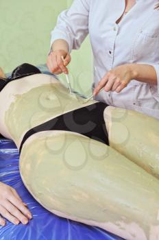 Woman having clay body mask apply by beautician