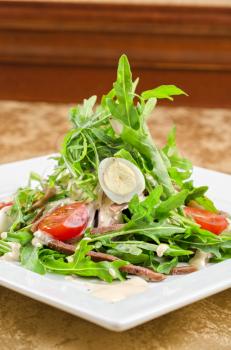 Tasty salad of beef tongue with eggs, arugula, tomato, spices and sauce
