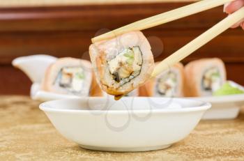 hand holding sushi with chopsticks at table