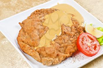 Delicious Schnitzel with lemon, tomato, lettuce and sauce.