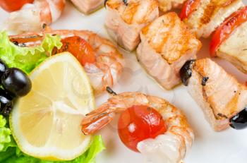 Closeup of grilled shrimps and tomatoes on bamboo sticks with salmon