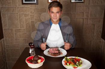 man holding a knife and a fork ready to eat a beef steak